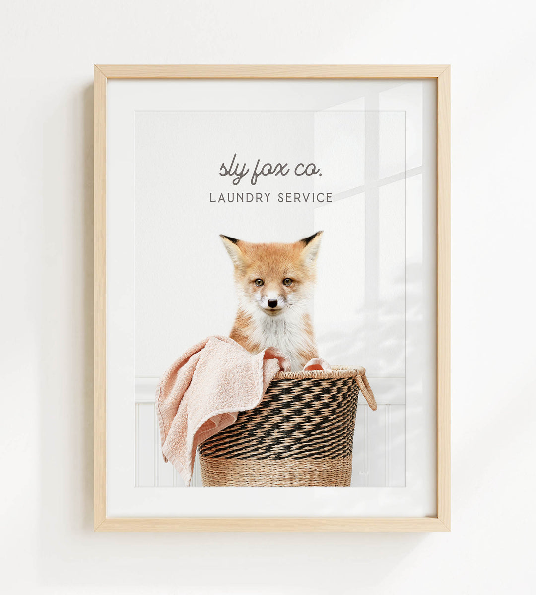 A framed image of a young fox sitting in a woven laundry basket, with the text "sty fox co. Laundry service" displayed above the image.
