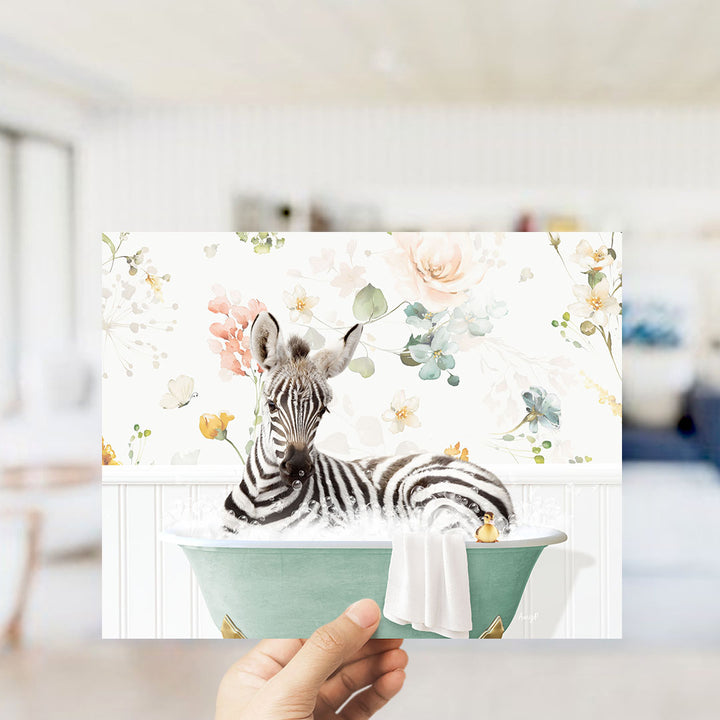 A hand is holding up a framed image of a zebra sitting in a bathtub, surrounded by a floral pattern.