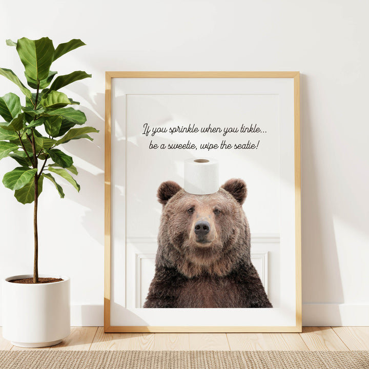 A framed image of a brown bear sitting on a roll of toilet paper, with a humorous caption that reads "If you sprinkle when youinkle... wipe the seat!"