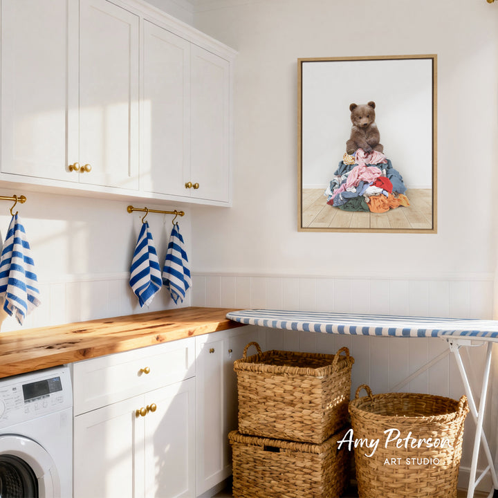 A cozy laundry room with white cabinets, a wooden countertop, and a framed image of a bear sitting on a pile of clothes.
