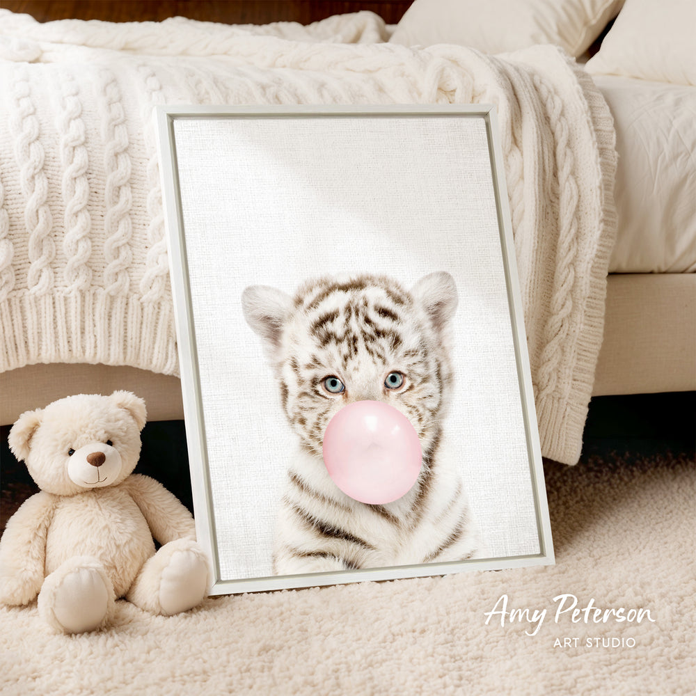 A framed print of a tiger blowing a bubble gum bubble is displayed on a beige carpet, accompanied by a teddy bear.