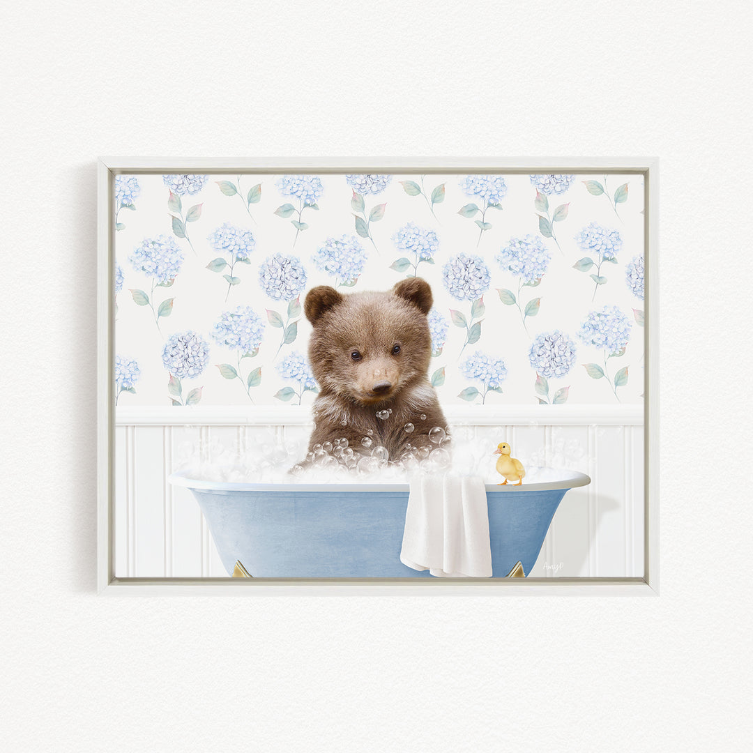 A brown bear sitting in a blue bathtub filled with bubbles, with a yellow duck floating nearby.