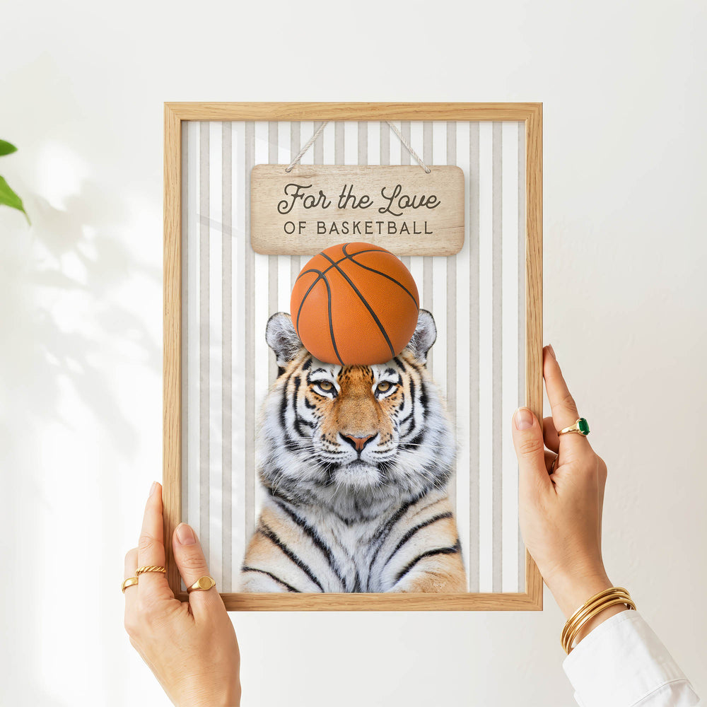 A person's hands are holding a framed picture of a tiger with a basketball on its head.