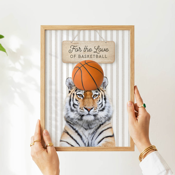 A person's hands are holding a framed picture of a tiger with a basketball on its head.