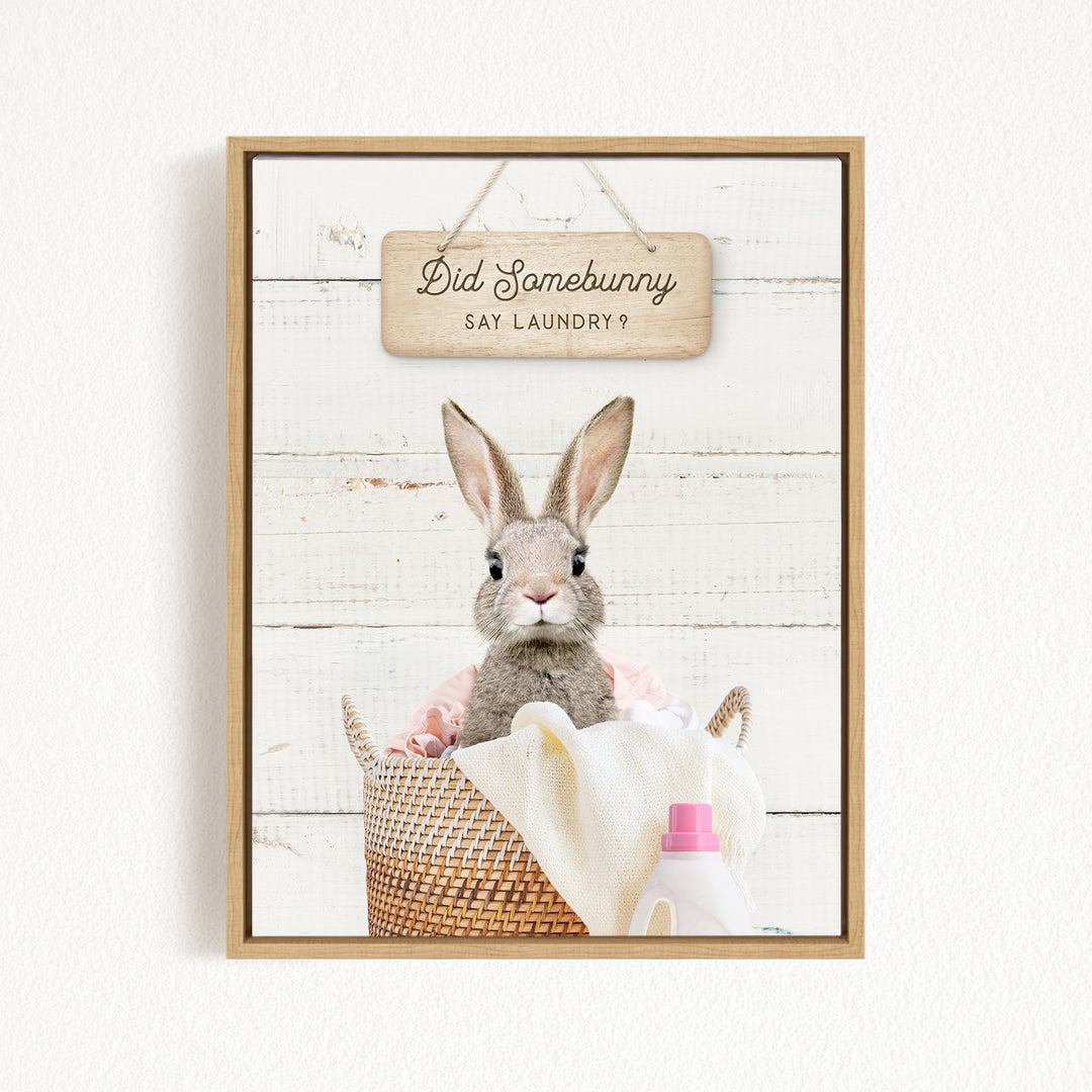 A cute rabbit sitting in a wicker basket filled with laundry, with a sign above that says "Did Somebunny Say Laundry?".
