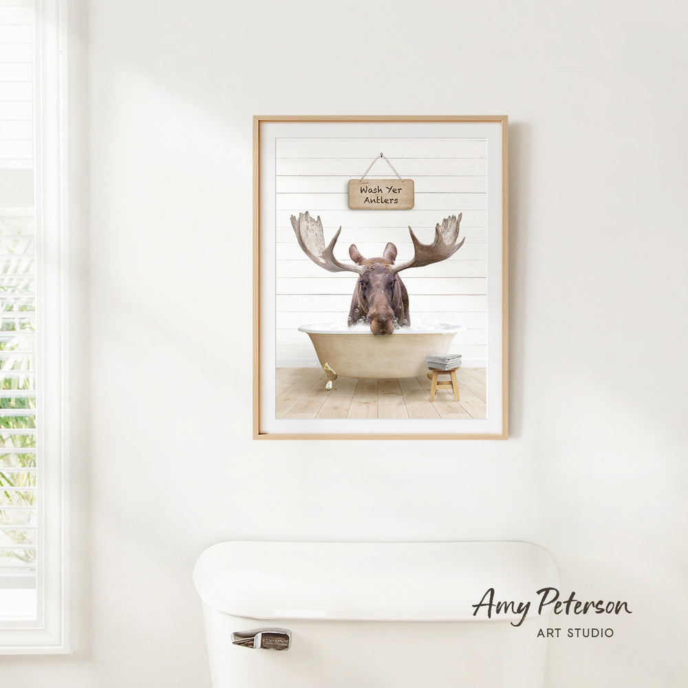 A framed image of a moose sitting in a bathtub, with a sign above it that says "Wash Your Antlers".