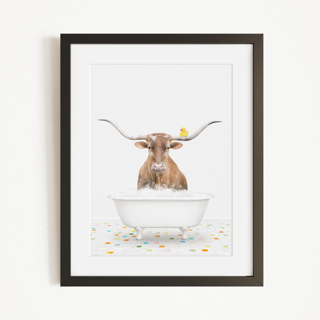A brown cow with large horns is sitting in a white bathtub filled with bubbles, with a yellow duck perched on its head.