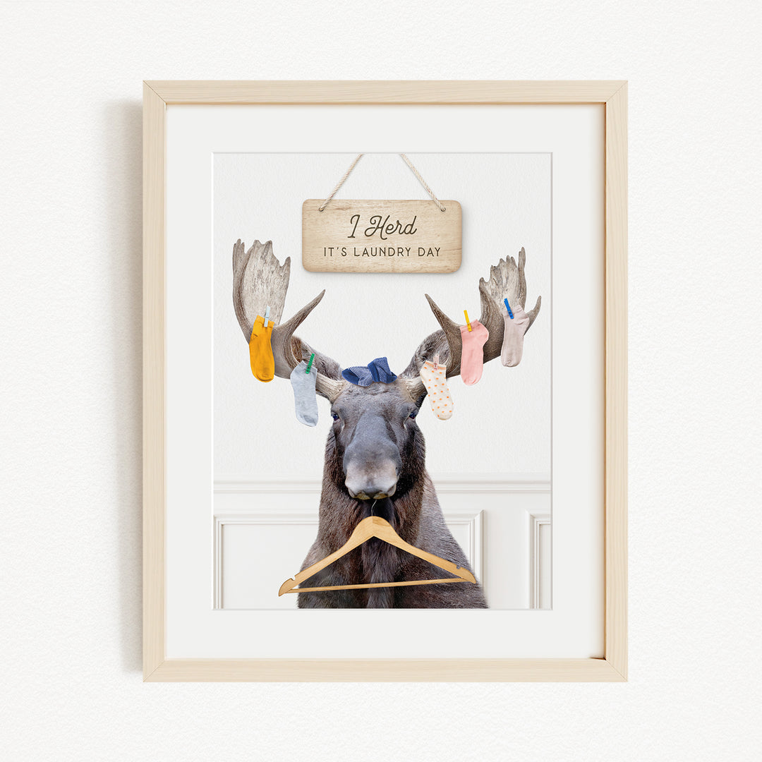 A framed image depicting a moose with a sign above it that says "I herd it's laundry day".