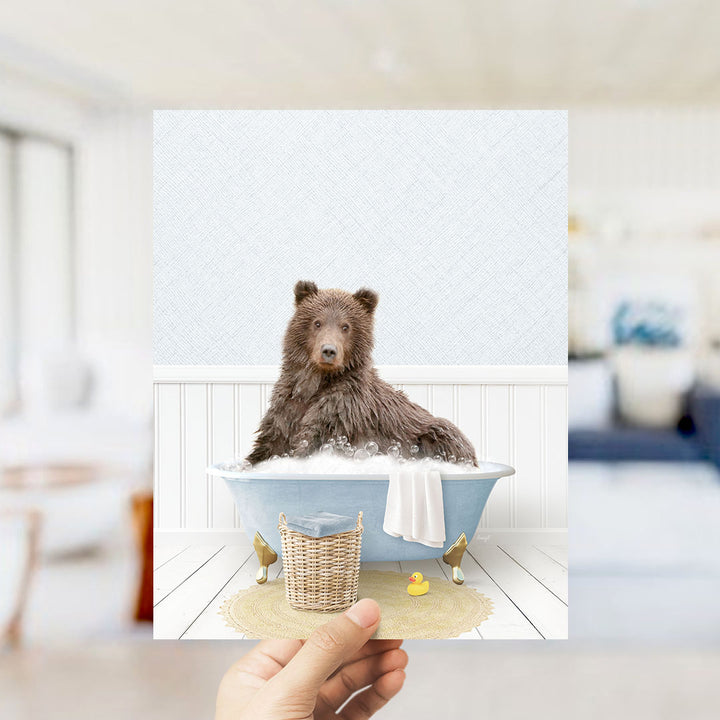A brown bear sitting in a blue bathtub filled with bubbles, surrounded by a yellow rubber duck and a white towel.