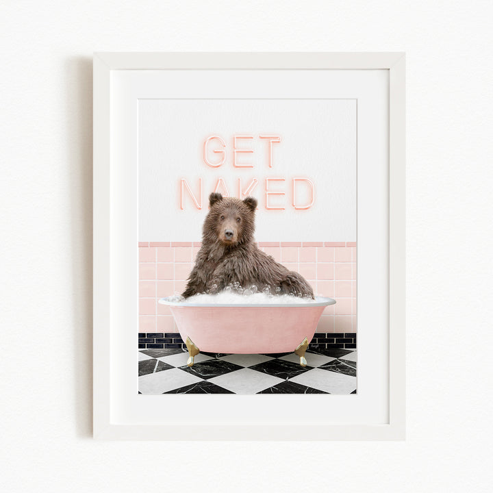 A brown bear sitting in a pink bathtub with the words "GET NAKED" written on the wall behind it.
