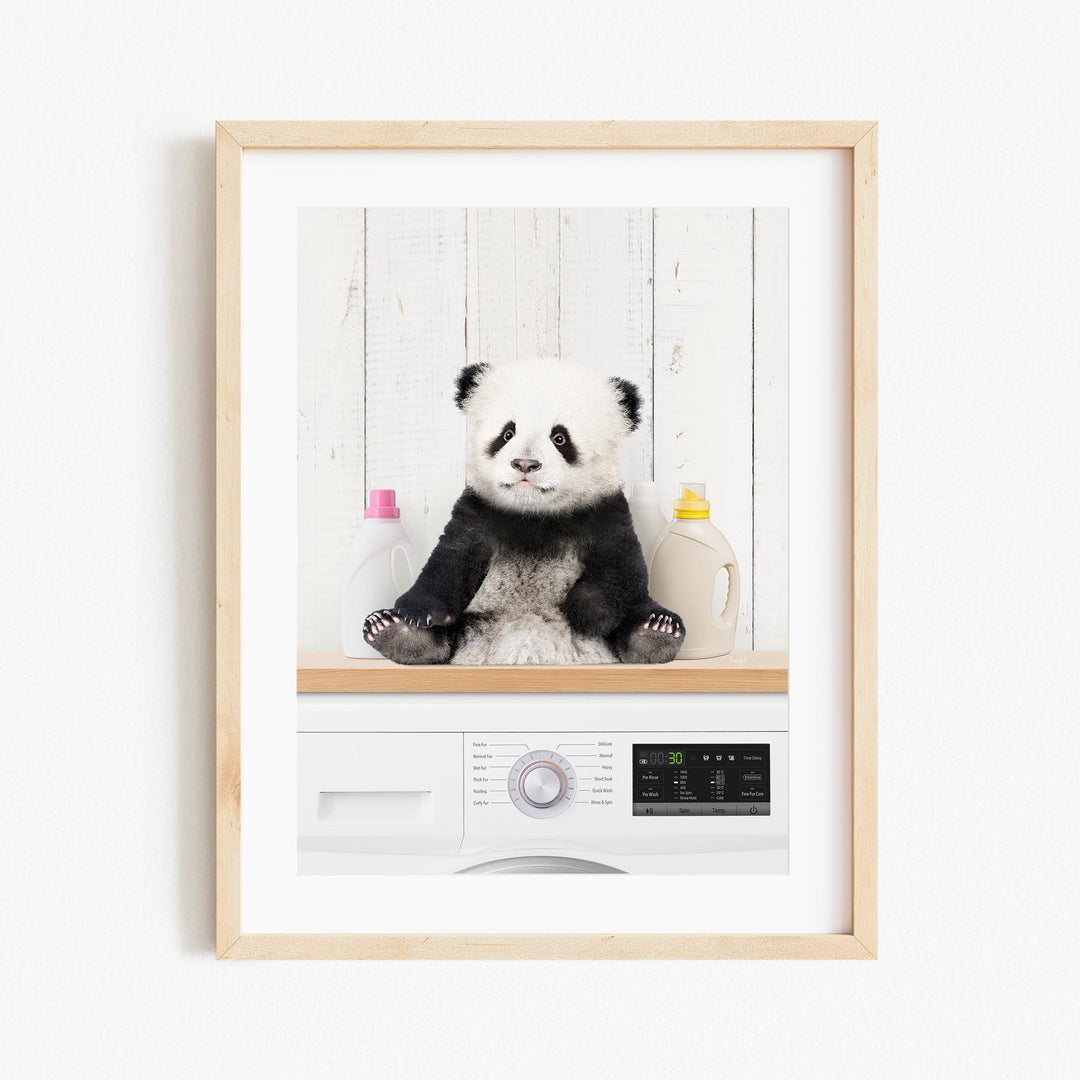 A panda bear sitting on a shelf next to a washing machine and two bottles of detergent.