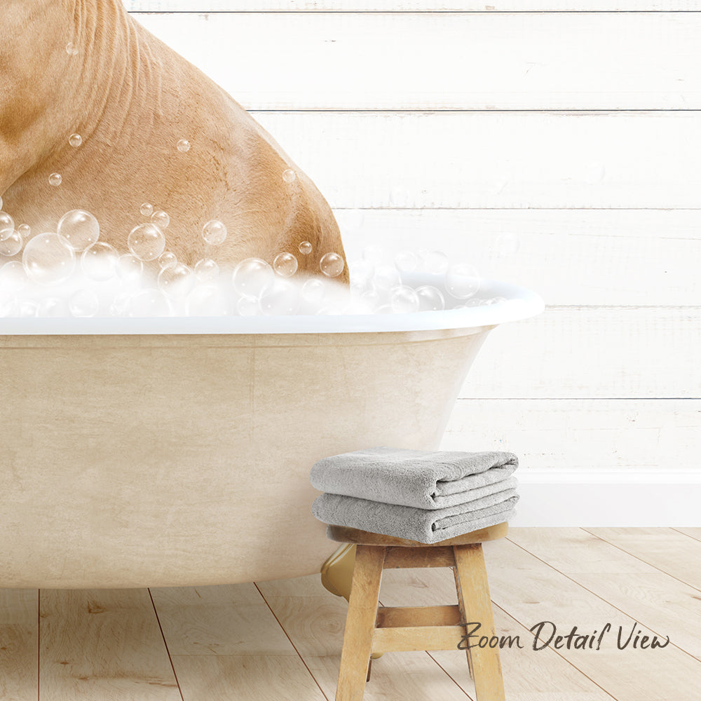 A dog is taking a bath in a white bathtub, surrounded by bubbles, with a towel and stool nearby.