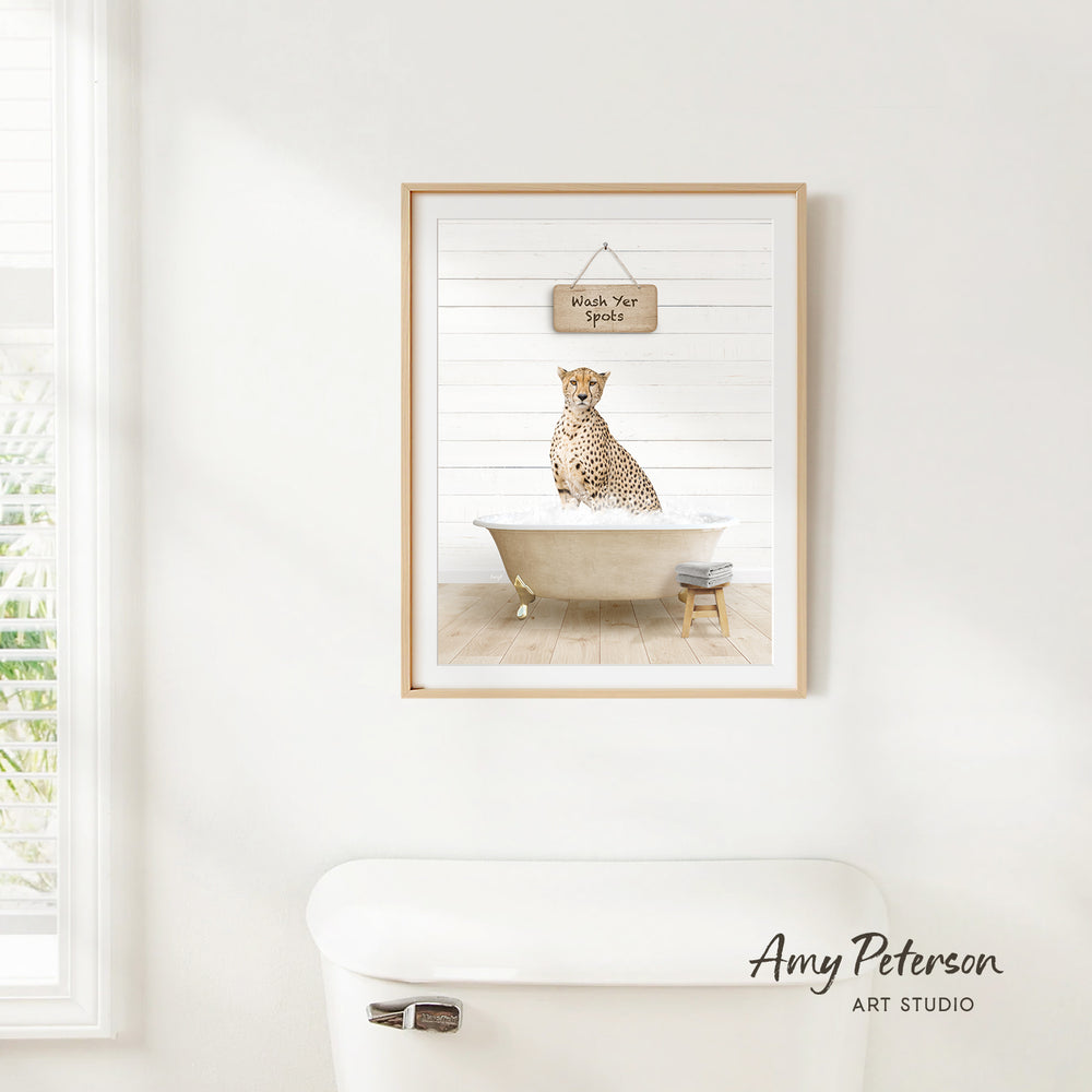 A framed print of a cheetah sitting in a bathtub, with a sign above it that says "Wash Your Spots".