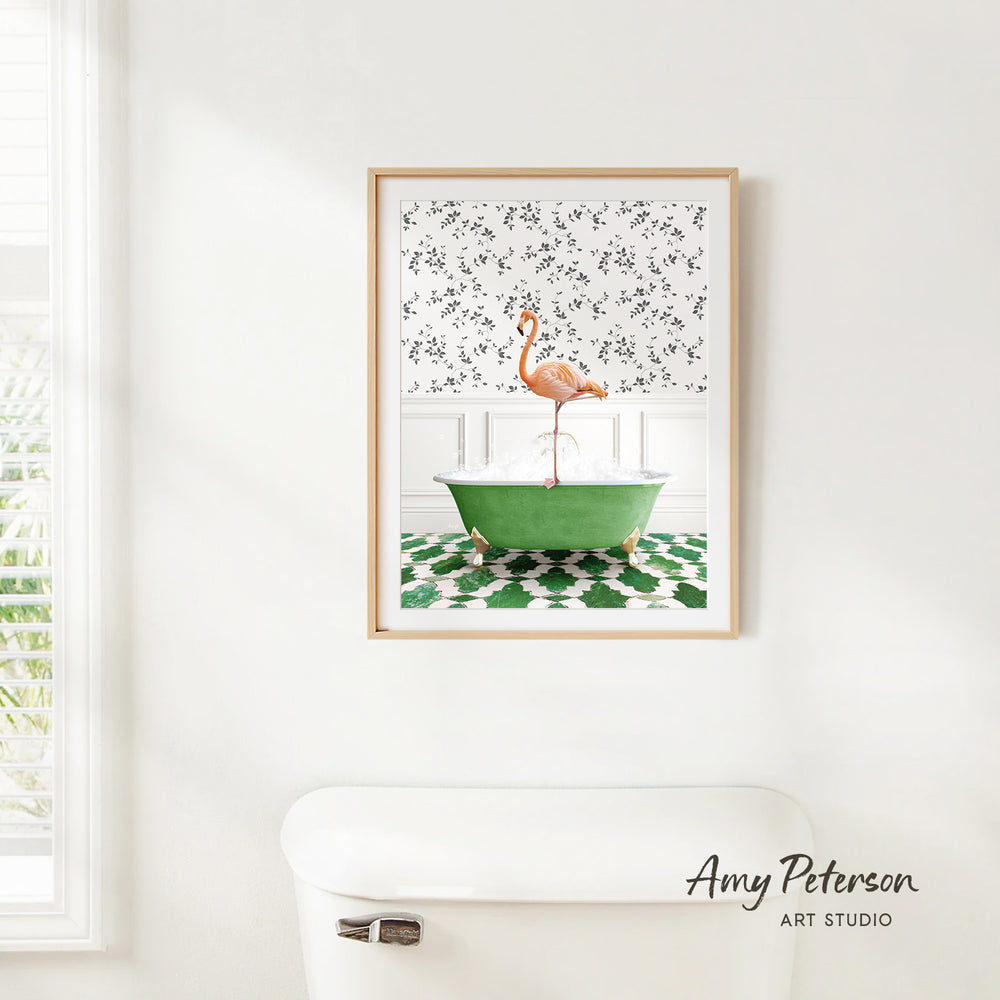 A framed print of a pink flamingo sitting in a green bathtub is hanging on a white wall in a bathroom.
