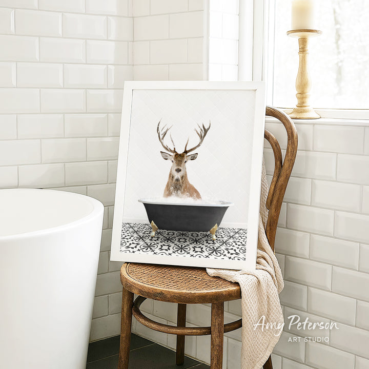 A framed image of a deer with antlers sitting in a bathtub, surrounded by a black and white patterned tile floor.
