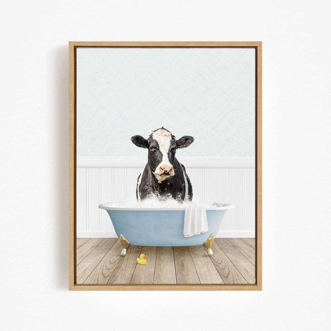 A black and white cow is sitting in a blue bathtub filled with water, surrounded by yellow rubber ducks.