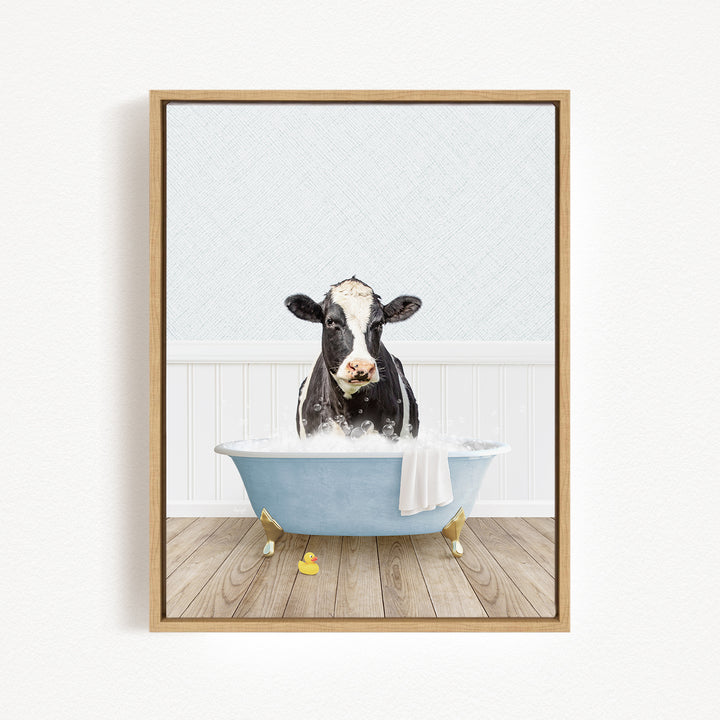 A black and white cow is sitting in a blue bathtub filled with water, surrounded by yellow rubber ducks.