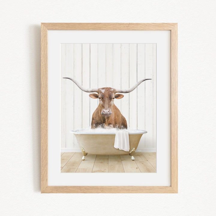 A framed image depicting a bull with large horns sitting in a bathtub filled with water.