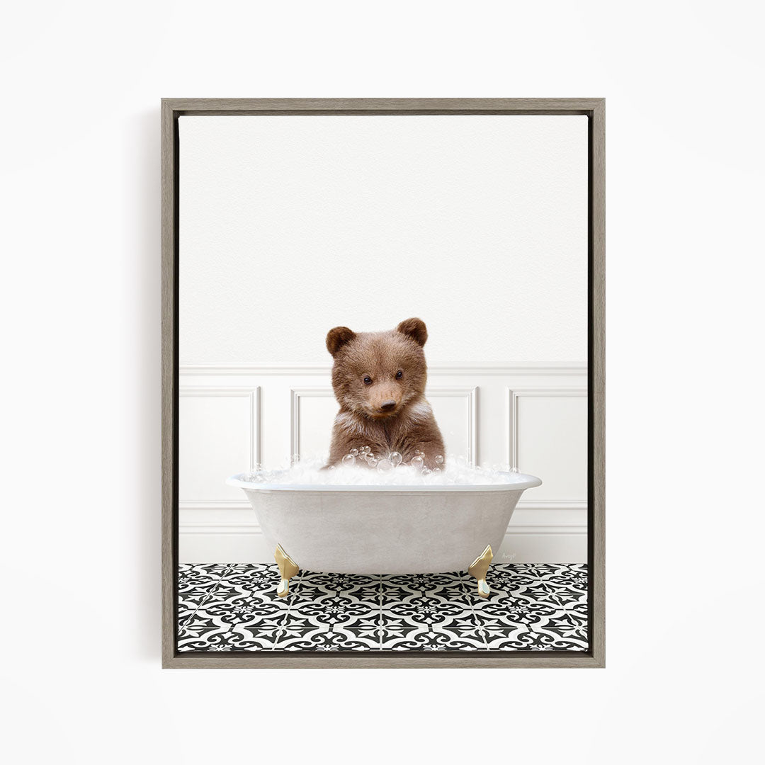 A brown bear sitting in a white bathtub filled with bubbles, looking directly at the camera.