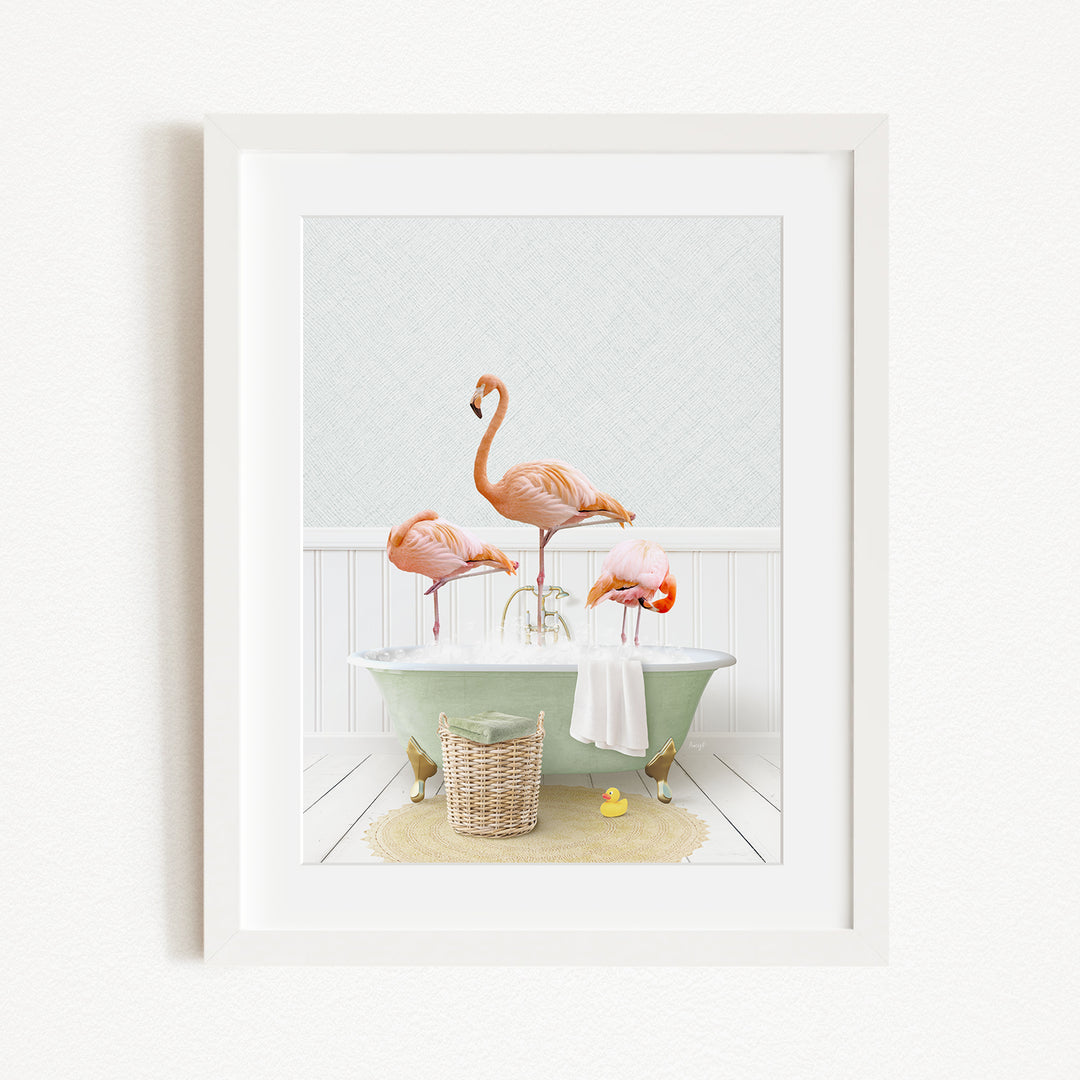 A framed image depicting three flamingos standing in a bathtub, with a basket of bath toys and a yellow rubber duck nearby.