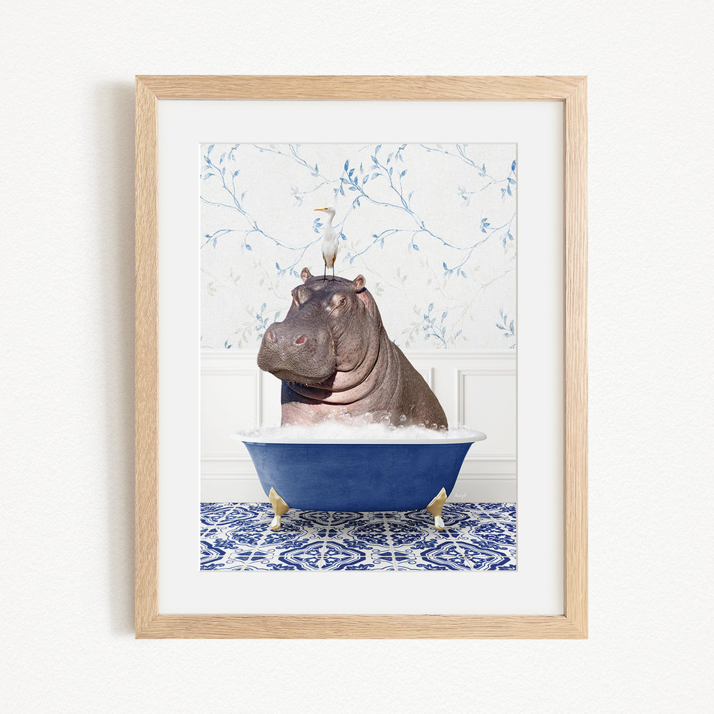 A framed image depicting a hippopotamus sitting in a blue bathtub, with a bird perched on its head.