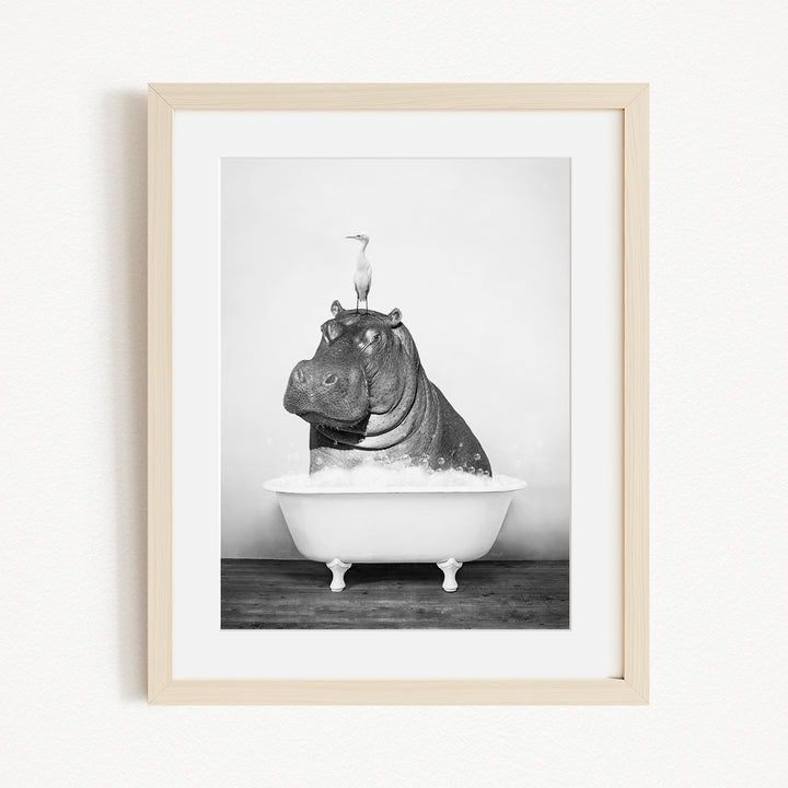 A black and white photograph of a hippopotamus sitting in a bathtub, with a bird perched on its head.