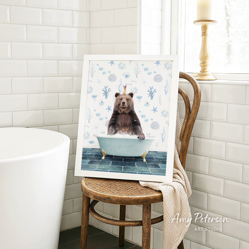 A framed image of a bear sitting in a bathtub, surrounded by blue and white floral patterns, is displayed on a wooden chair in a bathroom setting.