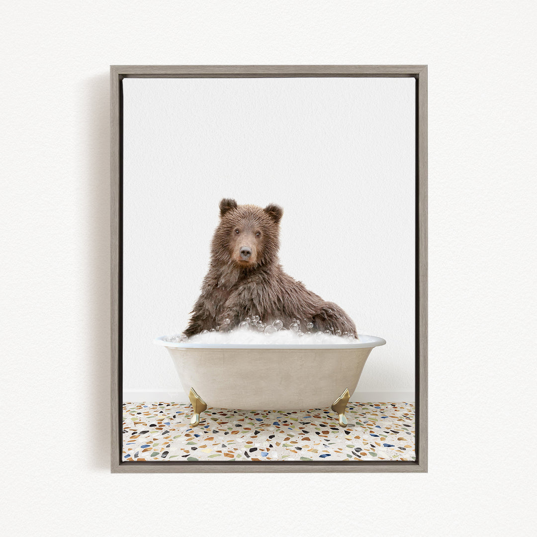 A brown bear sitting in a white bathtub filled with water, looking directly at the camera.
