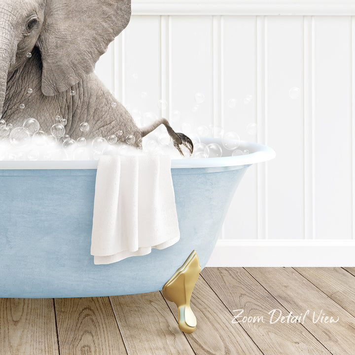A gray elephant is sitting in a blue bathtub filled with bubbles, with a white towel hanging on the side and a gold shoe placed on the floor next to the tub.