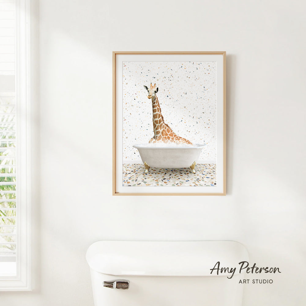 A framed painting of a giraffe sitting in a bathtub is hanging on a white wall.