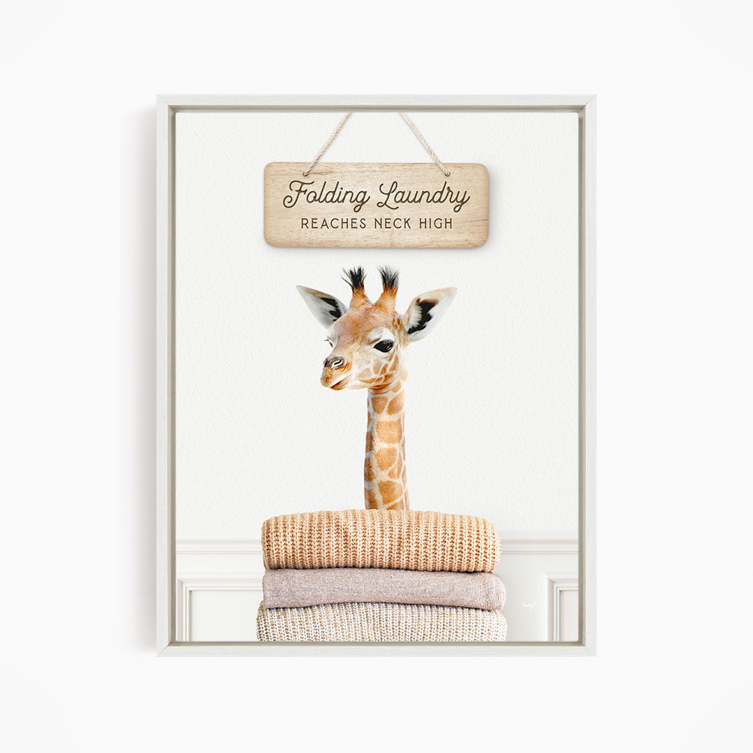A giraffe standing on a pile of folded clothes, with a wooden sign above that says "Folding Laundry Reaches necks high".