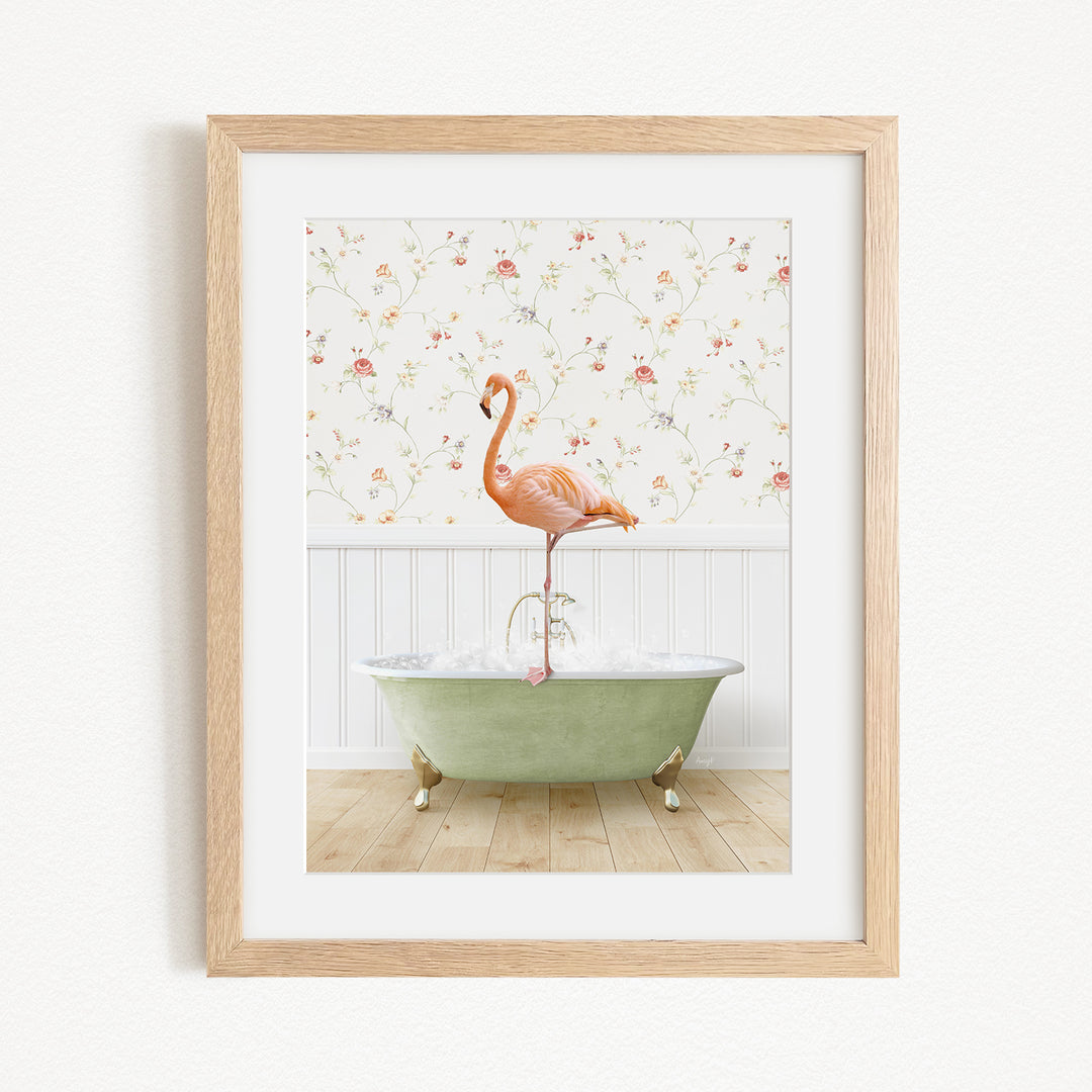 A framed image depicting a pink flamingo standing on the edge of a green bathtub filled with water, set against a floral wallpaper background.