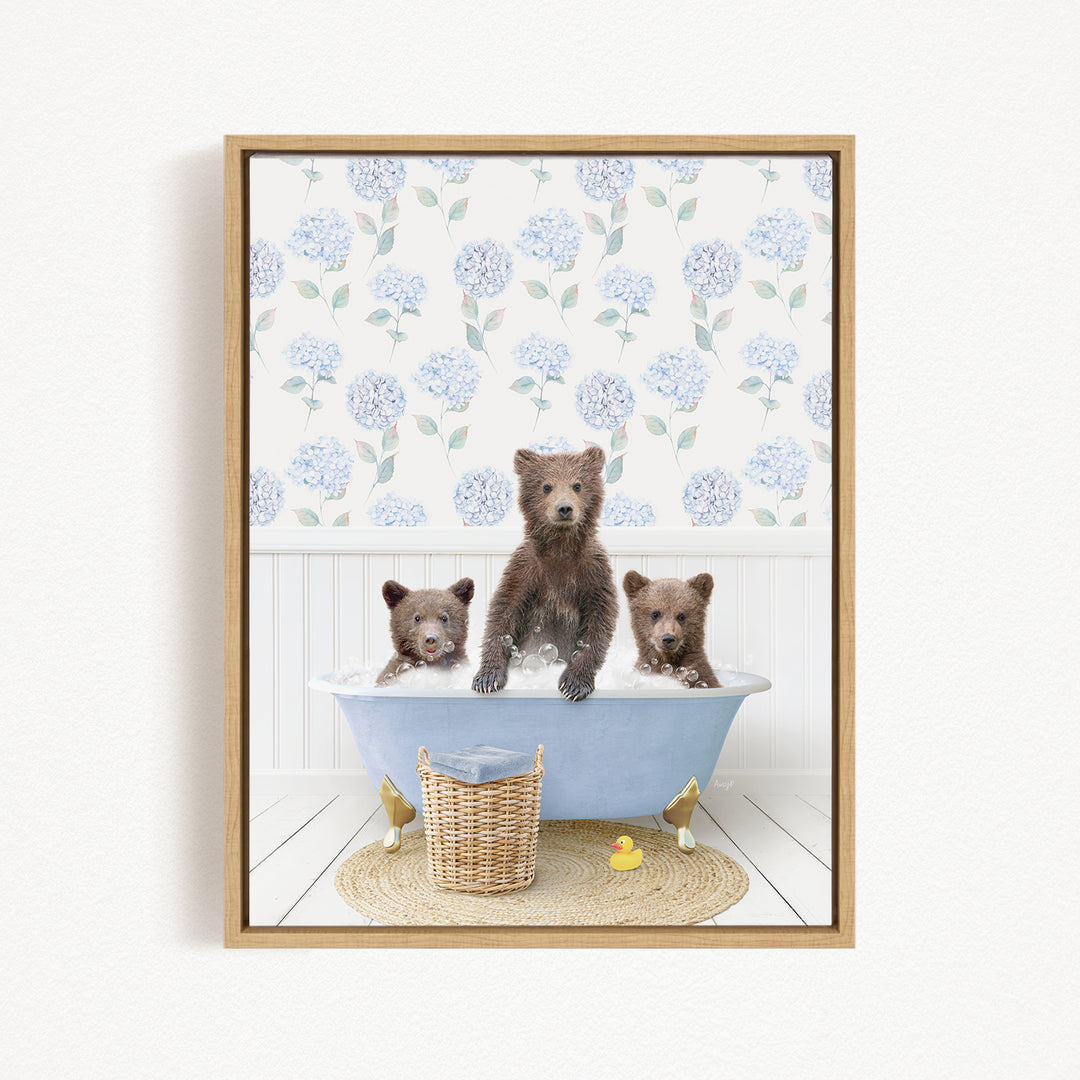 A framed image depicting three brown bears sitting in a blue bathtub, with a blue and white floral pattern on the wall behind them.