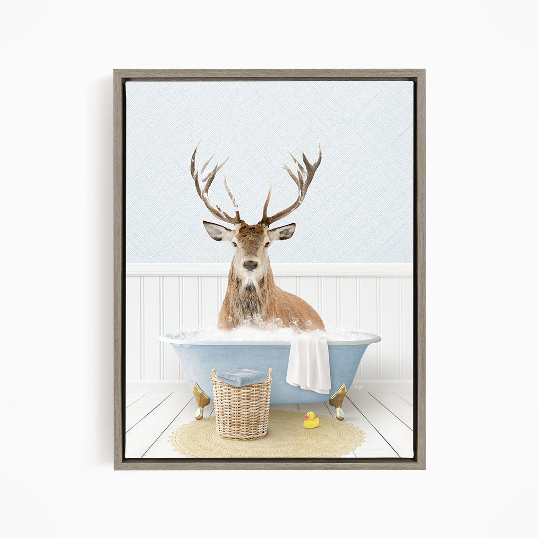 A deer with large antlers is sitting in a blue bathtub filled with bubbles, surrounded by rubber ducks and a basket.