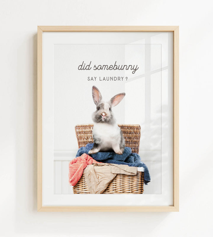 A gray and white rabbit sitting in a wicker basket filled with clothes, with the text "did some bunny say laundry?" displayed above the image.