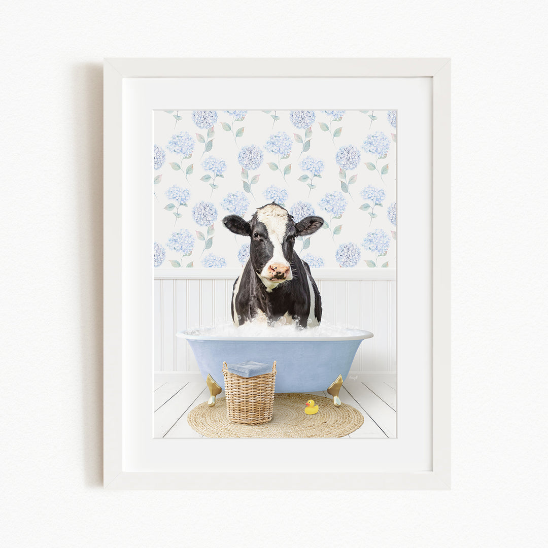 A black and white cow is sitting in a blue bathtub filled with water, surrounded by a floral patterned wall and a basket of rubber ducks.