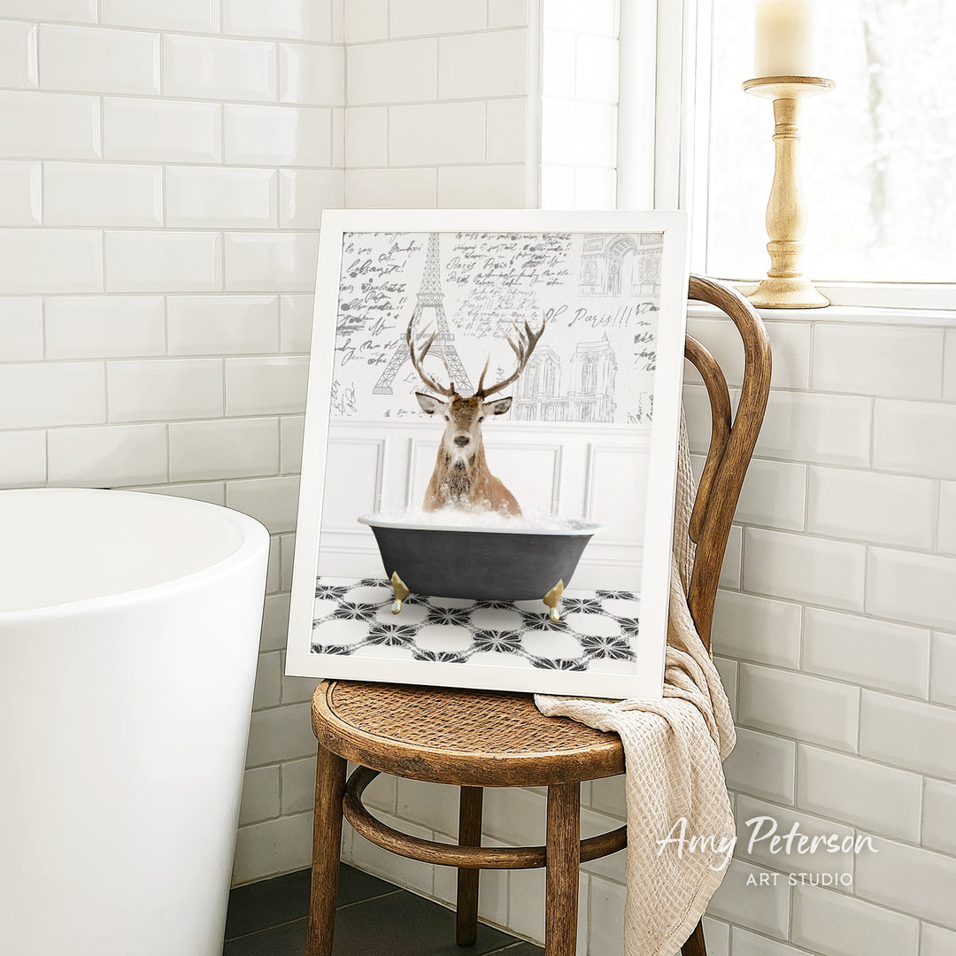 A framed image of a deer sitting in a bathtub, surrounded by a tiled pattern, is displayed on a wooden chair in a bathroom setting.