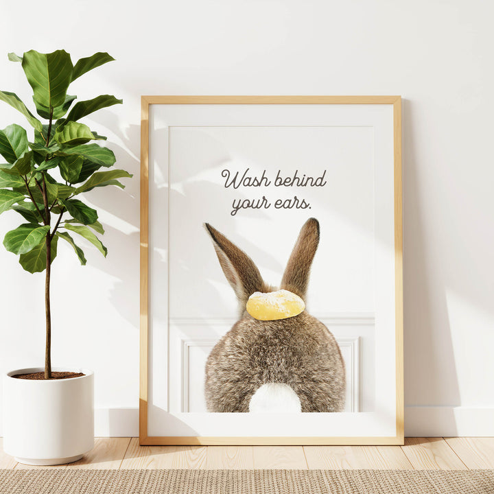 A framed poster with a picture of a rabbit's back, along with the text "Wash behind your ears" written on it.