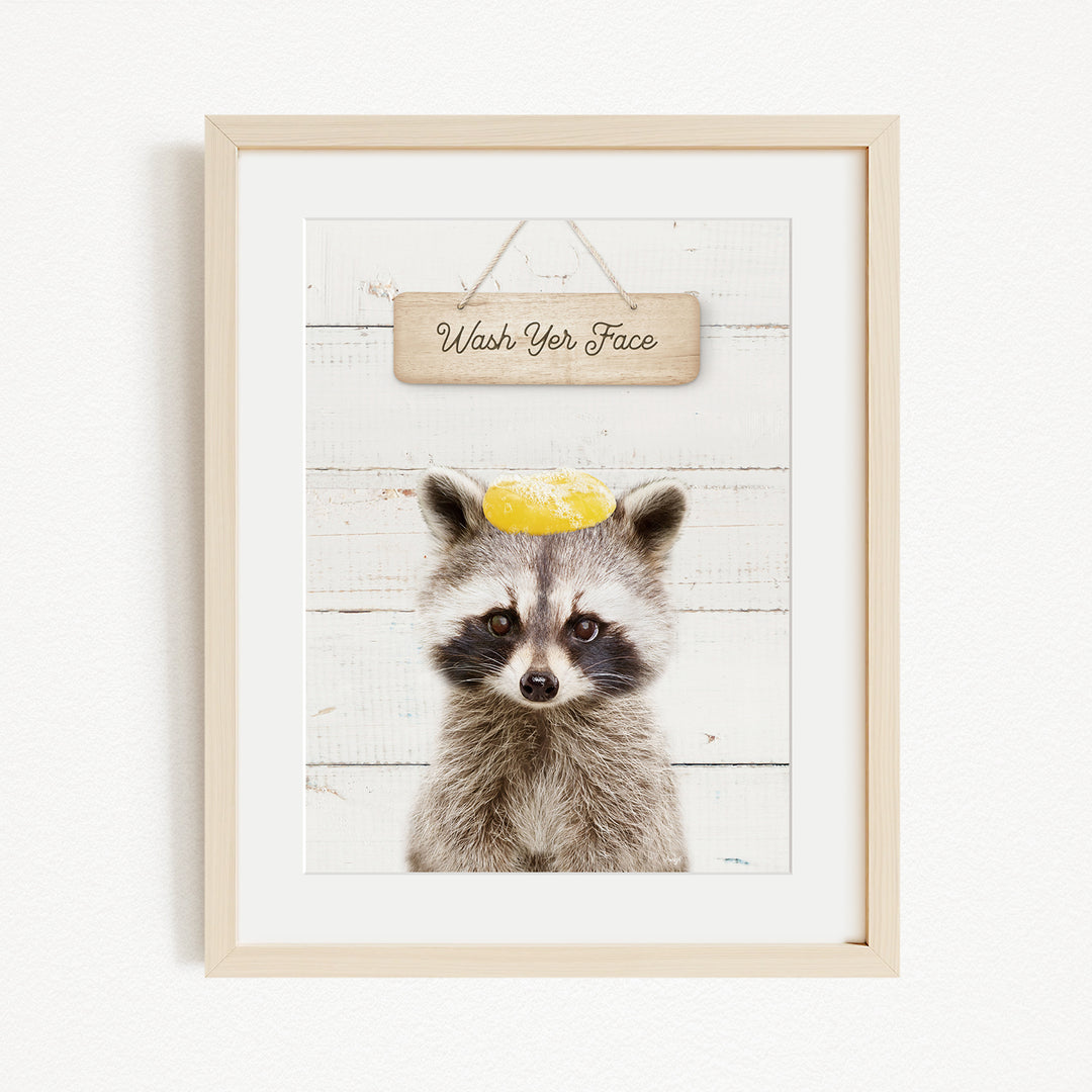 A raccoon wearing a yellow hat with the text "Wash Your Face" written on it, set against a white wooden background.