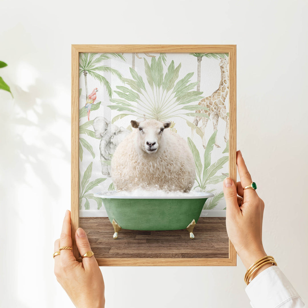 A person's hands are holding a framed picture of a sheep sitting in a green bathtub, surrounded by tropical foliage.