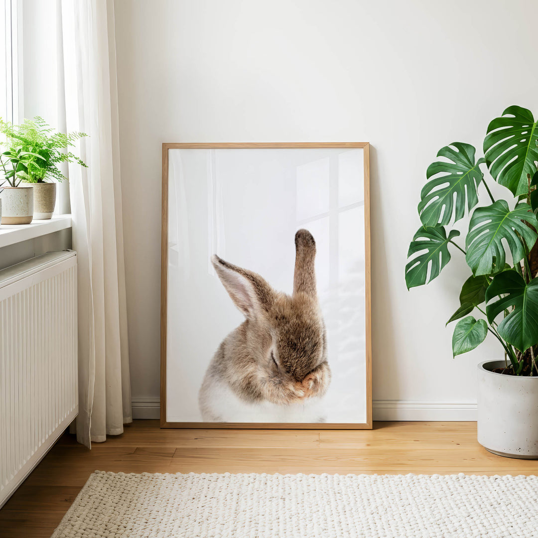 a large picture of a rabbit sitting on a wooden floor, with a white curtain and a potted plant in the background.