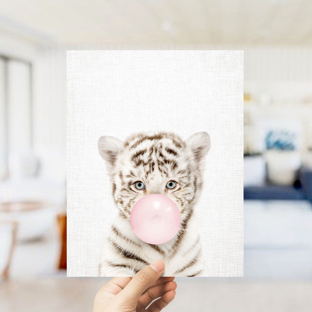 A hand is holding up a framed photograph of a tiger blowing a bubble with a pink bubble gum bubble.