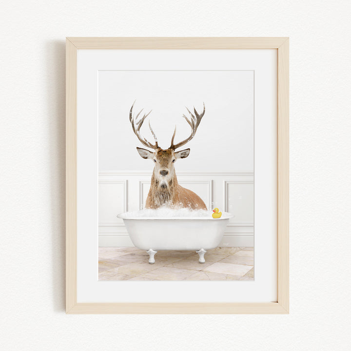 A deer with large antlers is sitting in a white bathtub filled with water, with a yellow rubber duck floating in the water.