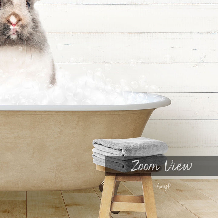 A fluffy white rabbit sitting in a bathtub filled with bubbles, with a wooden stool and towels nearby.