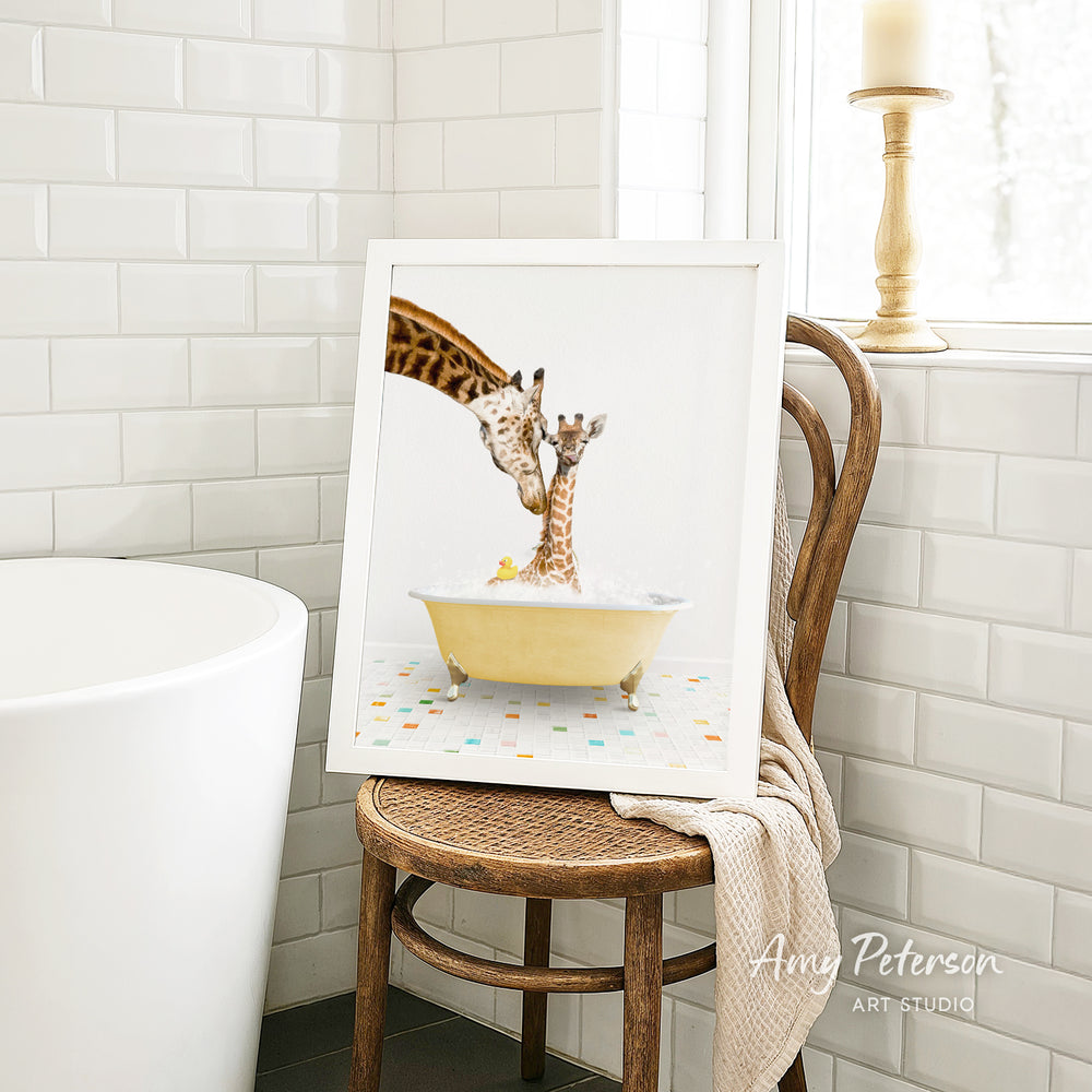 A framed image of a giraffe and a baby giraffe sitting in a yellow bathtub, with a towel draped over the back of a wooden chair in a bathroom setting.