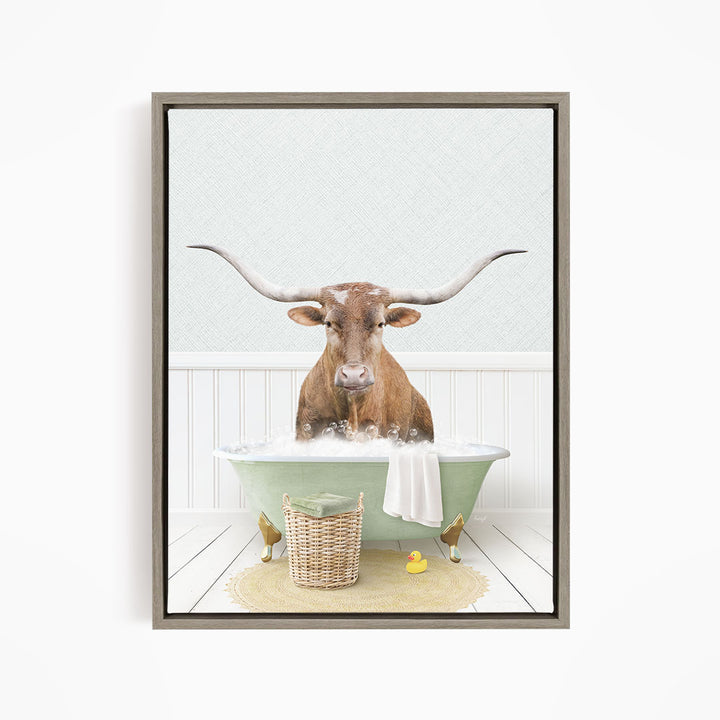 A brown bull with long horns is sitting in a green bathtub filled with bubbles, surrounded by a basket of rubber ducks and a towel.