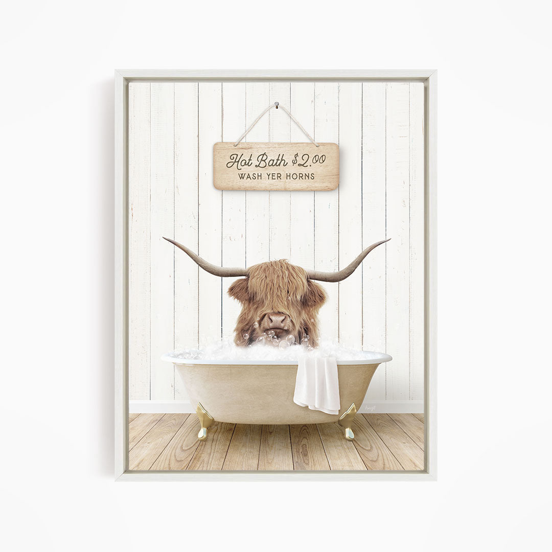 A framed image depicting a Highland cow with large horns sitting in a bathtub, with a sign above the bathtub that reads "Hot Bath $2.00 WASH YER HORSES".