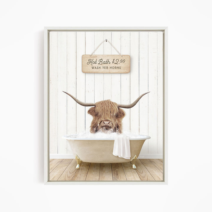 A framed image depicting a Highland cow with large horns sitting in a bathtub, with a sign above the bathtub that reads "Hot Bath $2.00 WASH YER HORSES".