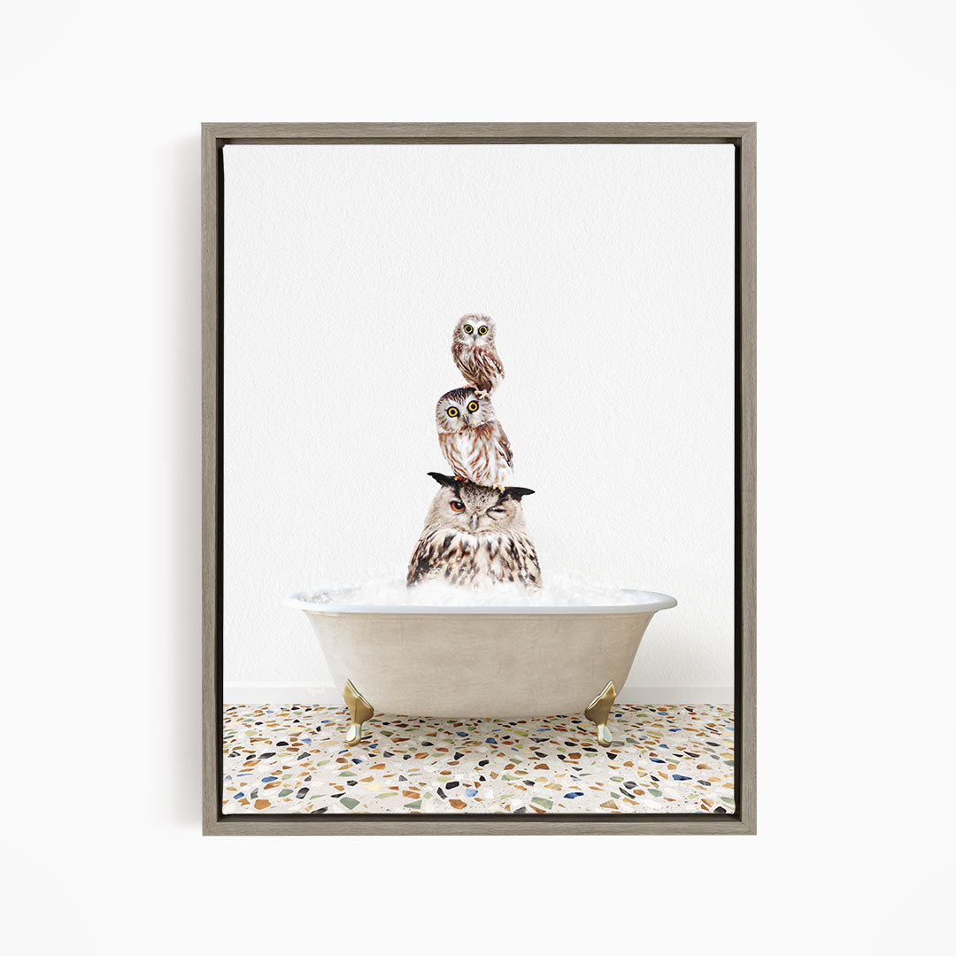 A framed image depicting three owls sitting in a bathtub, with one owl perched on top of the other two.