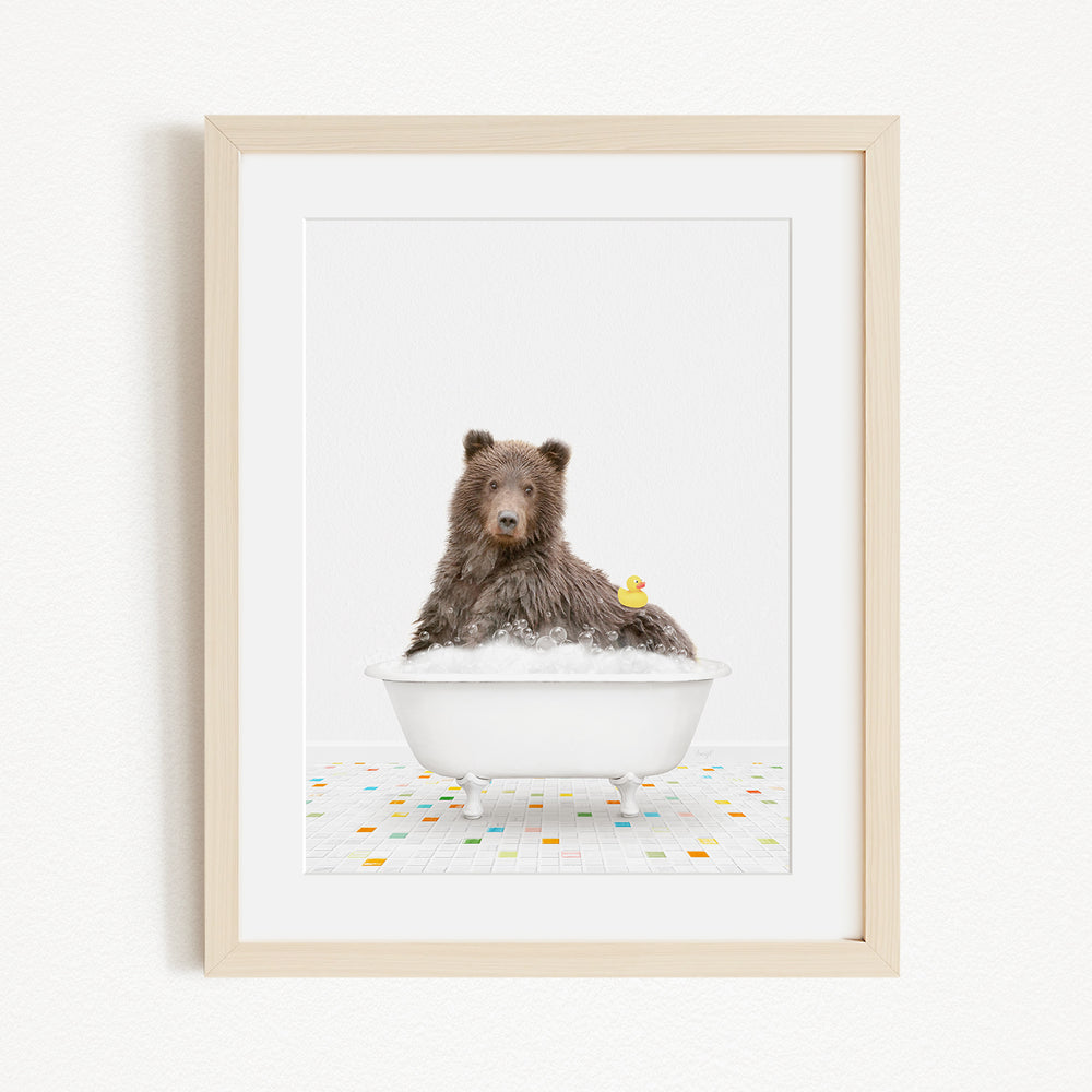 A brown bear sitting in a white bathtub filled with bubbles, with a yellow rubber duck floating nearby.